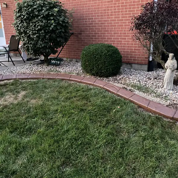 Curved concrete curb along a rock bed in front of a brick house