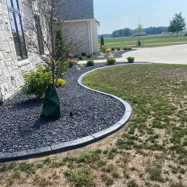 Curved concrete curb around a black rock bed beside a stone wall